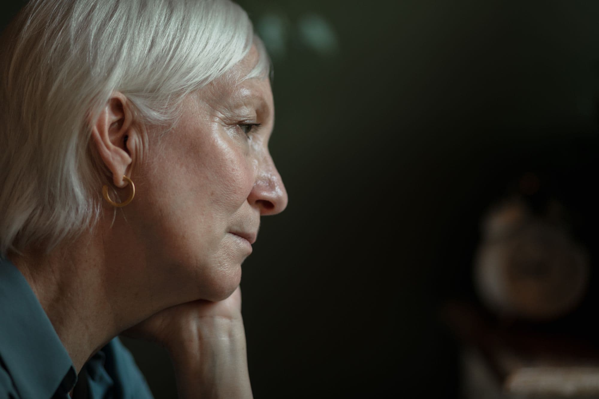 A woman in her sixties resting her chin on her hand, looking away in thought