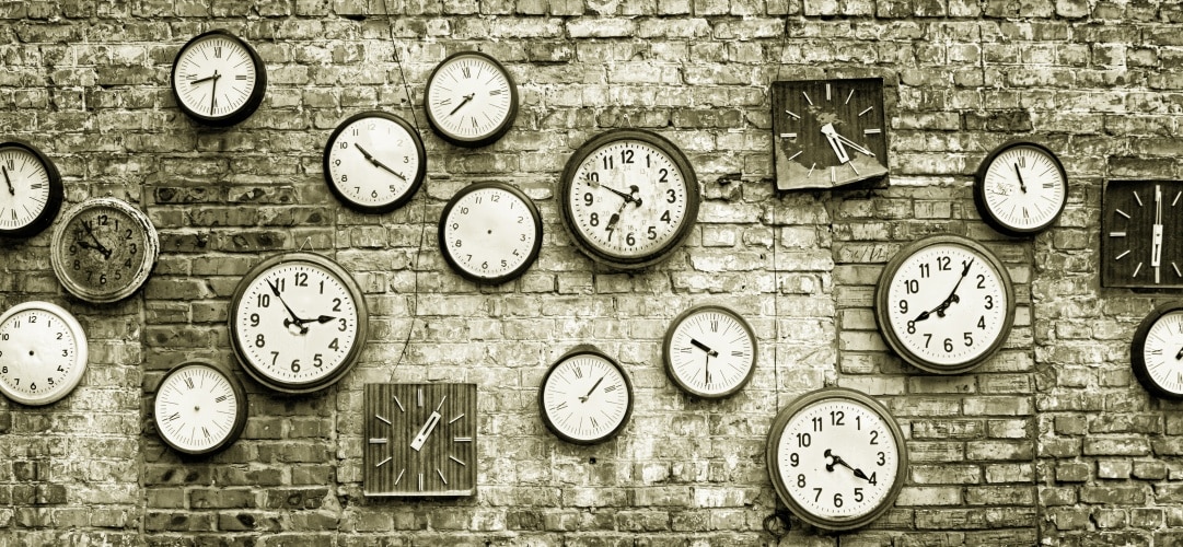 black and white photo of brick wall with lots of clocks hanging on it
