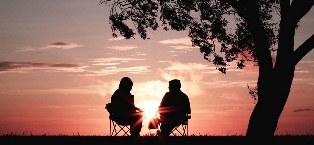 Couple sitting in lawn chairs under a tree looking at a sunset; representing retiring to Virginia